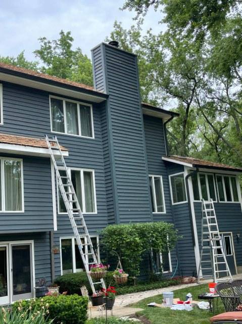 Dark blue home with chimney and ladders staged for exterior roofline work by GutterForge