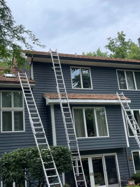 Dark blue home exterior with ladders set along the roofline for GutterForge exterior work