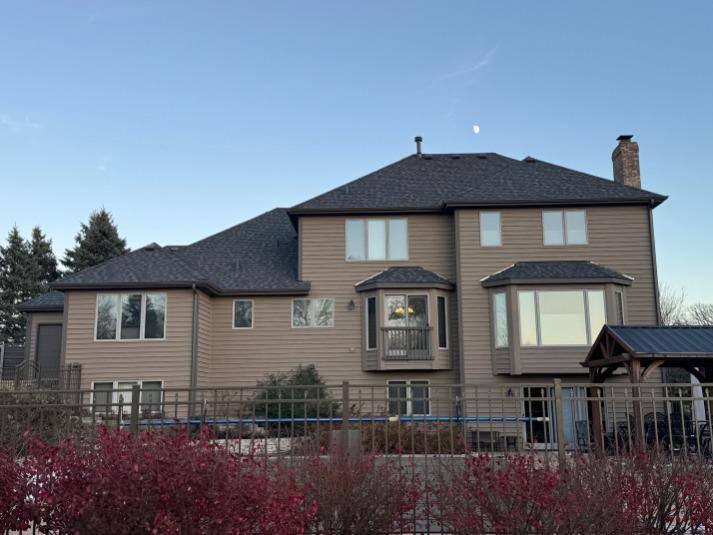 Tan two-story home exterior with upper roofline and gutters visible at evening